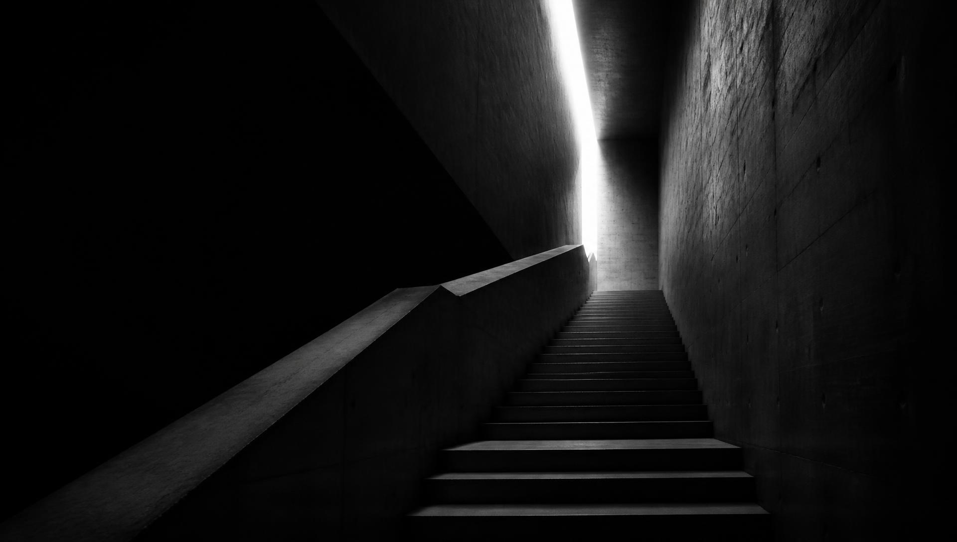 Escada de concreto ascendendo em direção a uma fresta de luz, em ambiente escuro